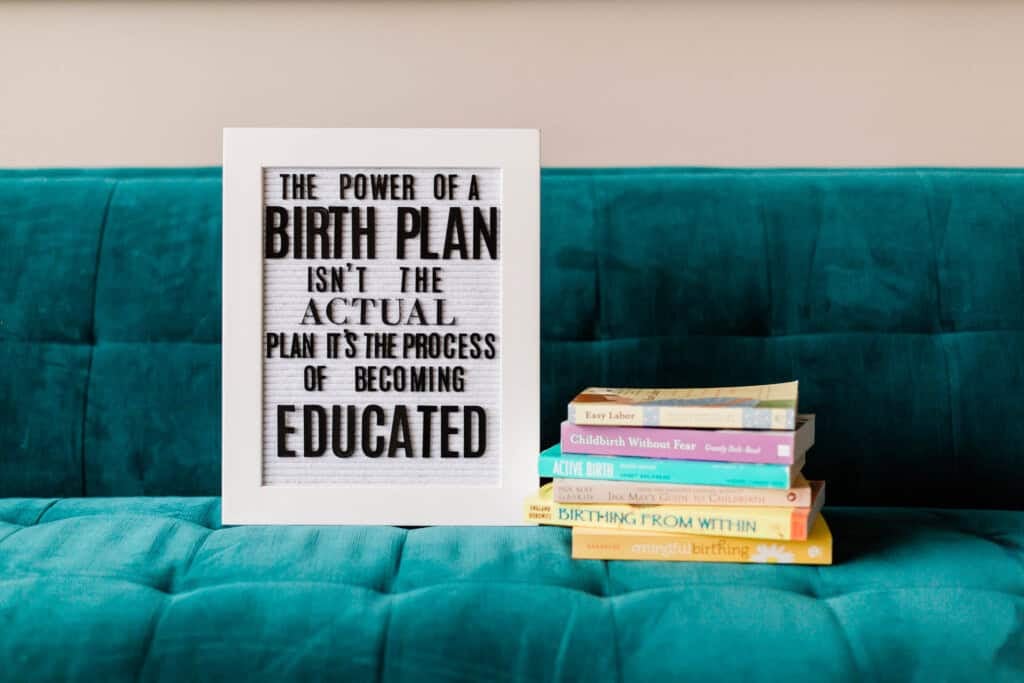 A framed sign with the quote The power of a birth plan isnt the actual plan. Its the process of becoming educated sits on a teal couch next to a stack of pregnancy and childbirth books&mdash;perfect inspiration to create your birth plan.