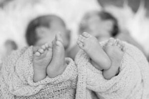 A black and white photo showing two babies lying down with their tiny feet pointing toward the camera. Both babies are wrapped in soft, knitted blankets, and their feet are closely positioned next to each other, capturing the precious moments before parents choose perfect names for twins.