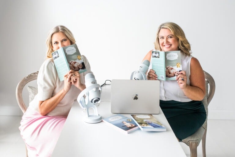 Two women sitting at a table, each holding up a book with an infant on the cover. They are positioned in front of an open laptop and two microphones, embodying the essence of Moms On Call. The background is plain white, creating a clean, simple setting.