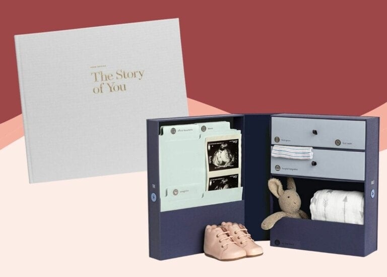 A navy blue keepsake box is displayed open, revealing compartments with baby items, including a stuffed bunny, baby shoes, ultrasound photos, and folded clothes. Adjacent is a closed white memory book titled "The Story of You" in gold font—one of the best baby books to cherish.