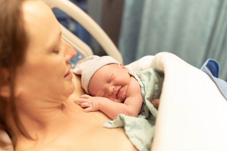 Mother holding a newborn baby close to her chest, both wrapped in the serenity of birth affirmations. The baby is swaddled in a blanket and wearing a small hat, as they rest peacefully in a hospital setting.
