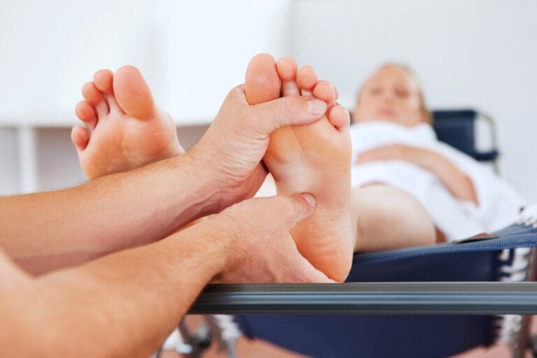 A person is receiving a foot massage while lying down, with the masseuse's hands focusing on massaging the soles. In the background, the individual lies comfortably on a cushioned surface, possibly a massage table. This technique can be particularly beneficial when using acupressure during labor.