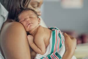 Here is your text with all single and double quote characters removed: A newborn sleeps on an adults bare shoulder, wrapped in a hospital blanket with green and red stripes. As they rest close together, they dream of sweet moments and choosing perfect baby boy names 2025 for the little one.