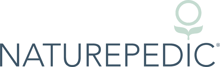 Logo of Naturepedic consisting of the word "NATUREPEDIC" in uppercase, dark blue letters, and a circular graphic above it featuring a white circle with two leaf shapes beneath it, all set against a transparent background. Choosing the right crib mattress is an important decision for parents, and the logo reflects that commitment to quality.